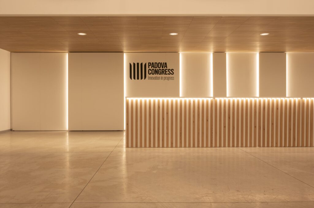 Primo piano del bancone reception in listelli di legno con retroilluminazione LED e logo "PADOVA CONGRESS Innovation in progress".