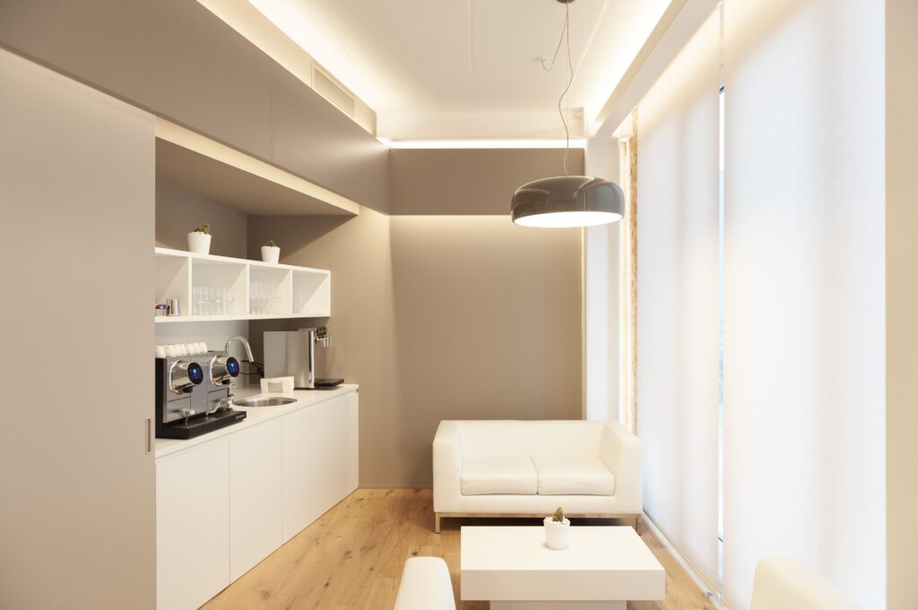 Area break dell'ufficio con tavoli alti e sgabelli bianchi, parquet in legno e ampie lampade a sospensione.